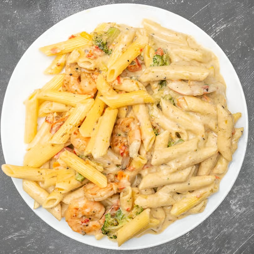 Creamy penne pasta with shrimp, broccoli, and red peppers on a white plate.